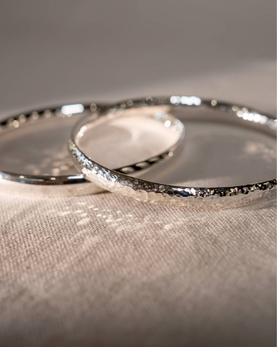 Close-up of two hammered silver bangles on textured fabric, handmade jewellery