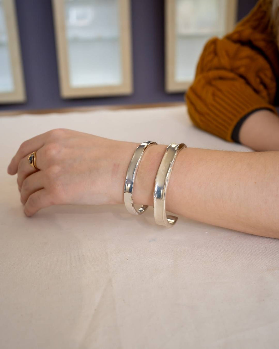 Hand wearing two hammered silver cuffs and a gold ring, jewelry on wrist, natural setting