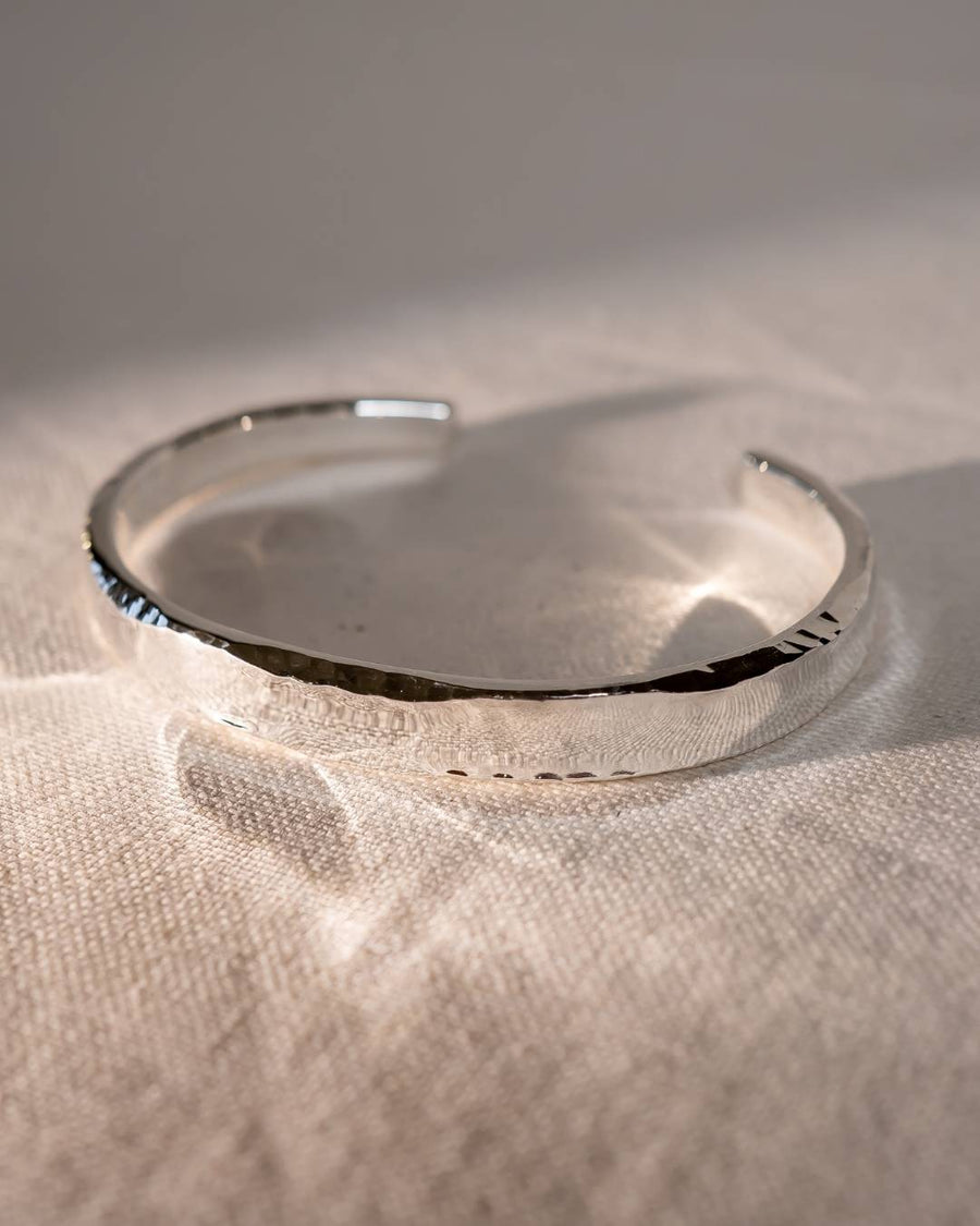 Handcrafted silver cuff bracelet with hammered texture on a soft fabric background