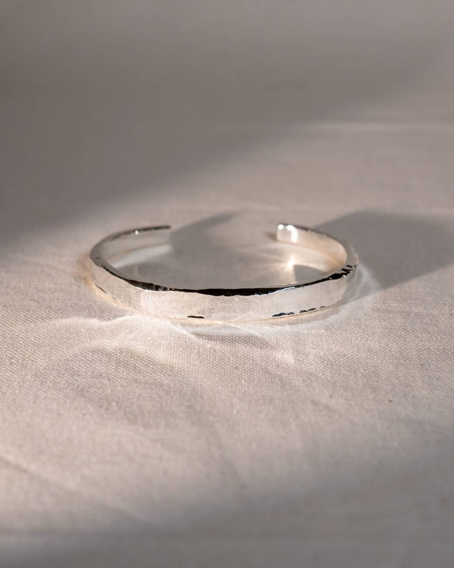 Handmade silver bangle with organic hammered texture on a soft fabric background