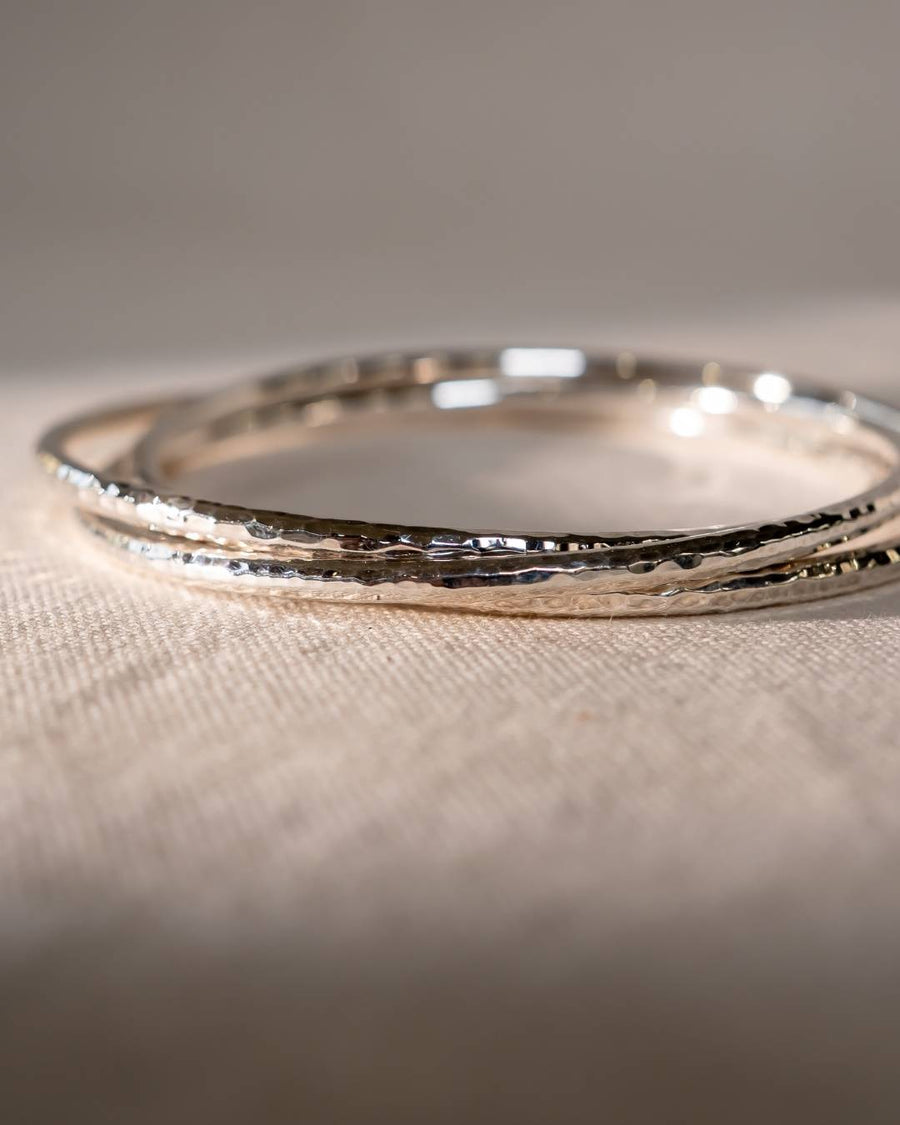 Handmade silver bangle bracelets with hammered textured finish on a neutral fabric surface