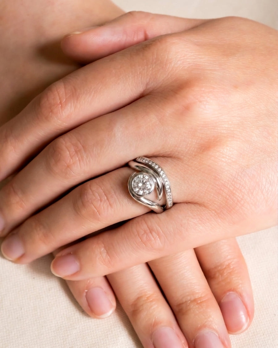 Silver spiky engagement ring with a round diamond and a diamond-shaped wedding band on a hand.
