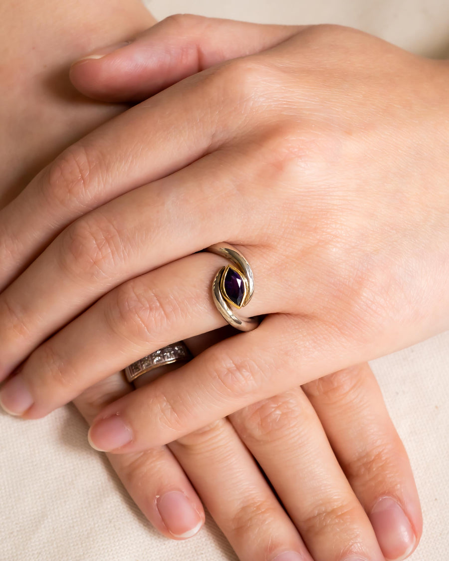 Silver and gold ring with a purple marquise gemstone on a hand.