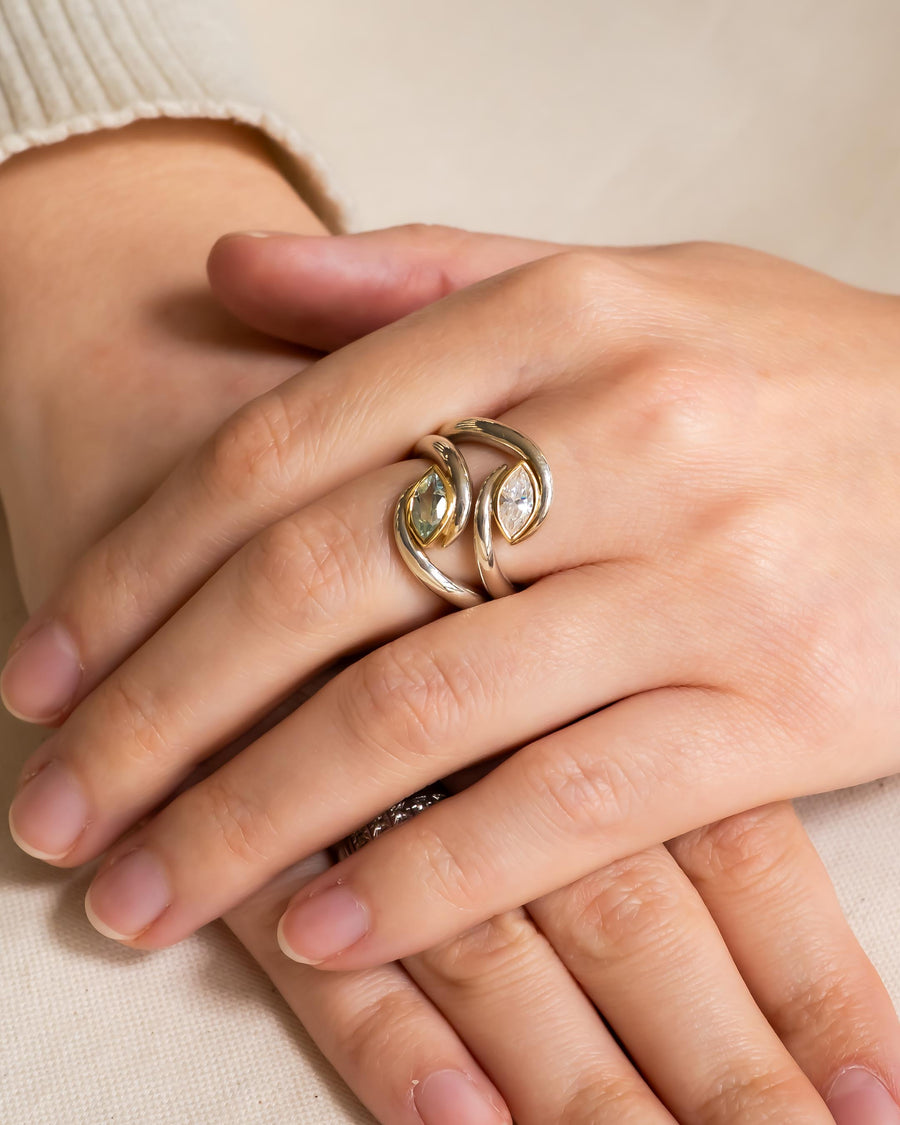 Silver and gold ring with two marquise-cut gemstones on a hand.