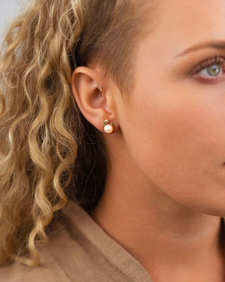 Gold stud earring with a spiky design holding a single pearl.