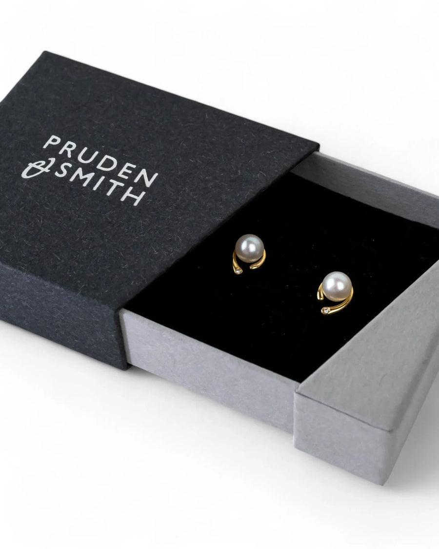 Gold pearl and diamond stud earrings in a black gift box.