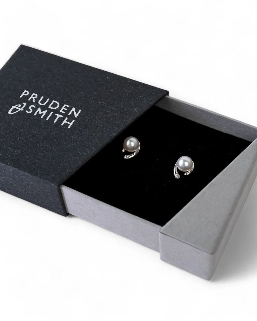Silver stud earrings with gray pearls and small diamonds, presented in an open black box.