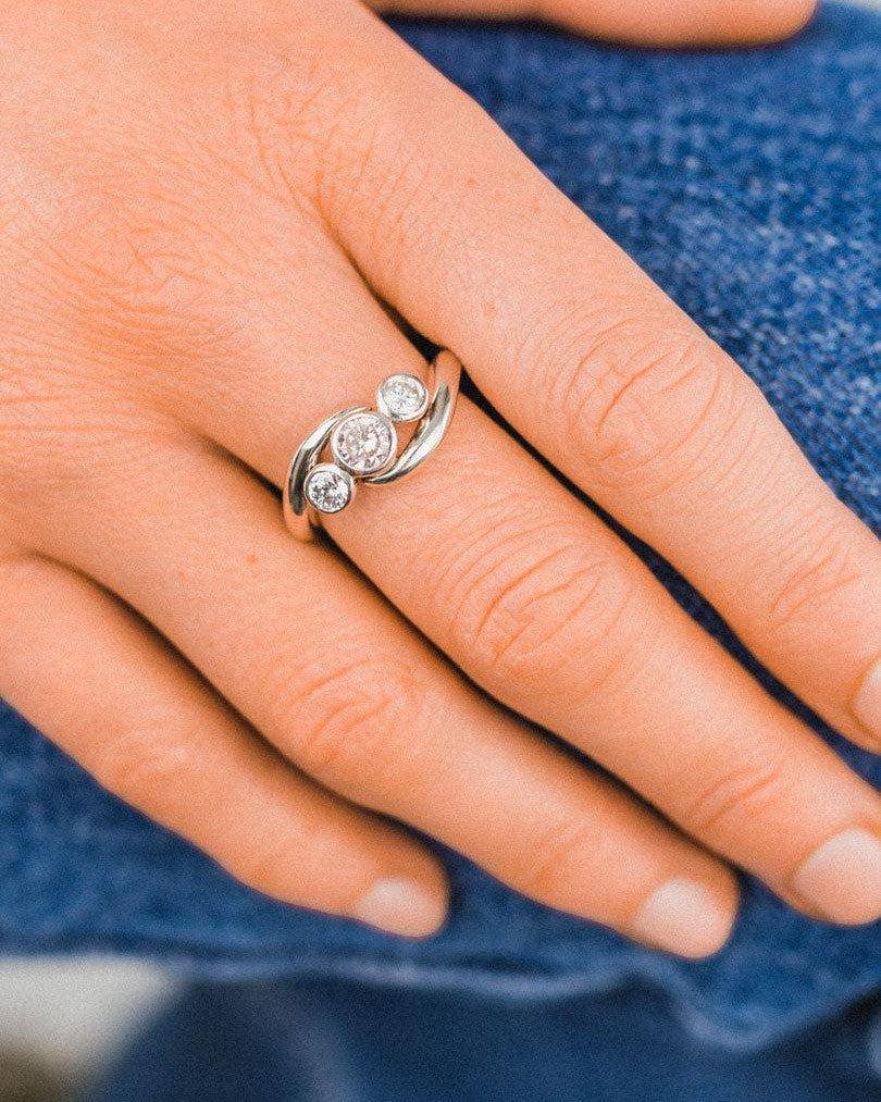 Hand wearing a platinum trilogy ring with three round diamonds, unique luxury jewelry design.