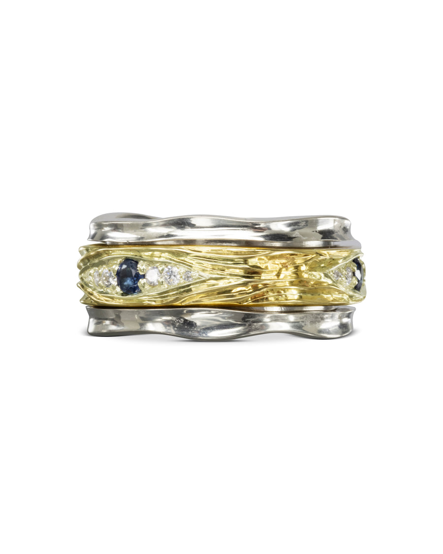 Two silver-toned bands sandwich a textured gold band with blue and clear gemstones.