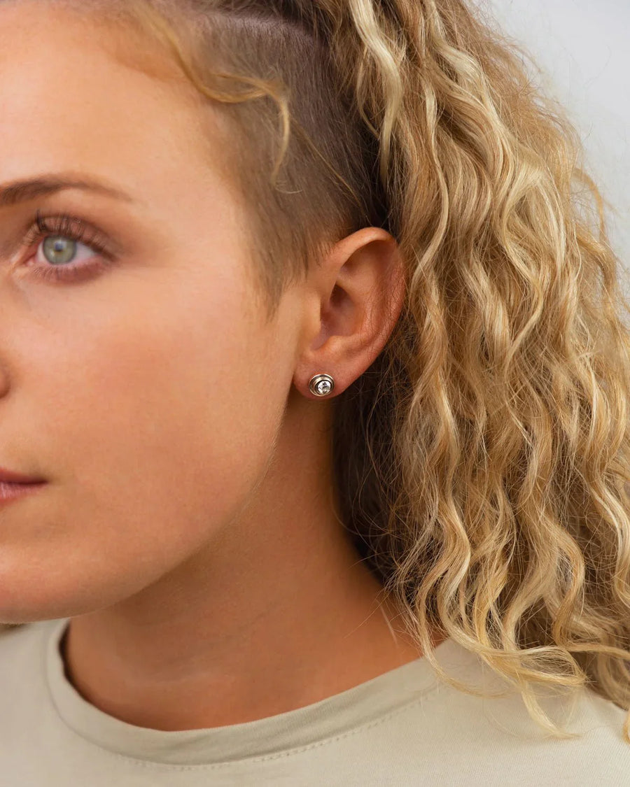 Silver spiral diamond stud earring on an ear.