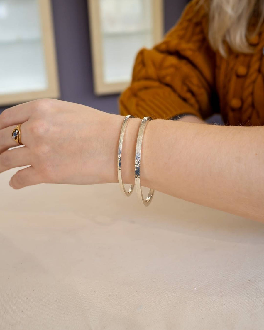 Hand wearing two hammered silver bangles with organic texture on a neutral background