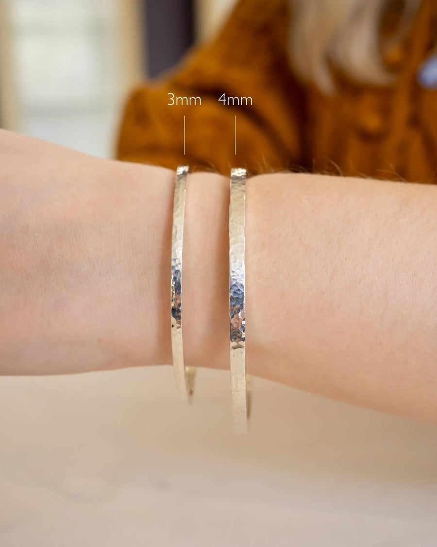 Two handcrafted hammered silver bangles, 3mm and 4mm wide, worn on a wrist