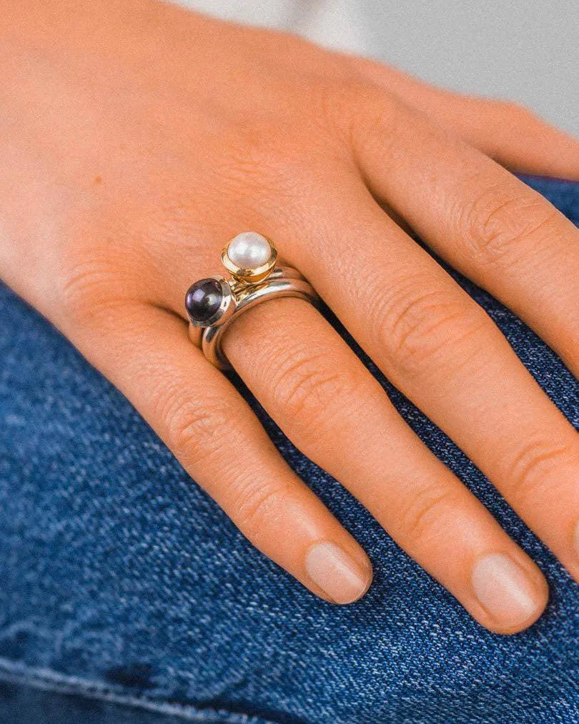 Stackable silver rings with a white pearl and a dark pearl.