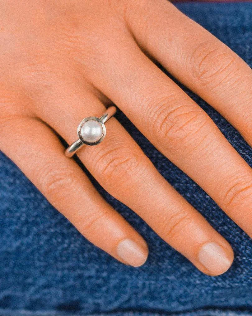 Silver ring with a single round white pearl on a hand.