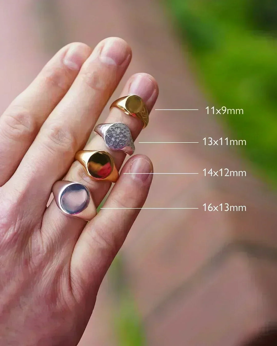 Hand wearing four signet rings in gold and silver, shown in different sizes outdoors