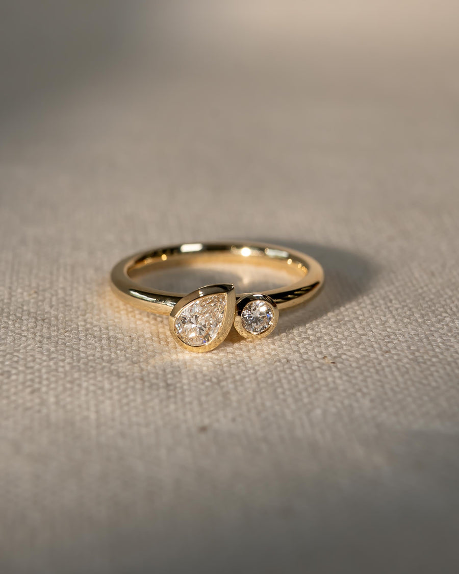 Gold toi et moi engagement ring with bezel-set pear and round diamonds on a textured surface.