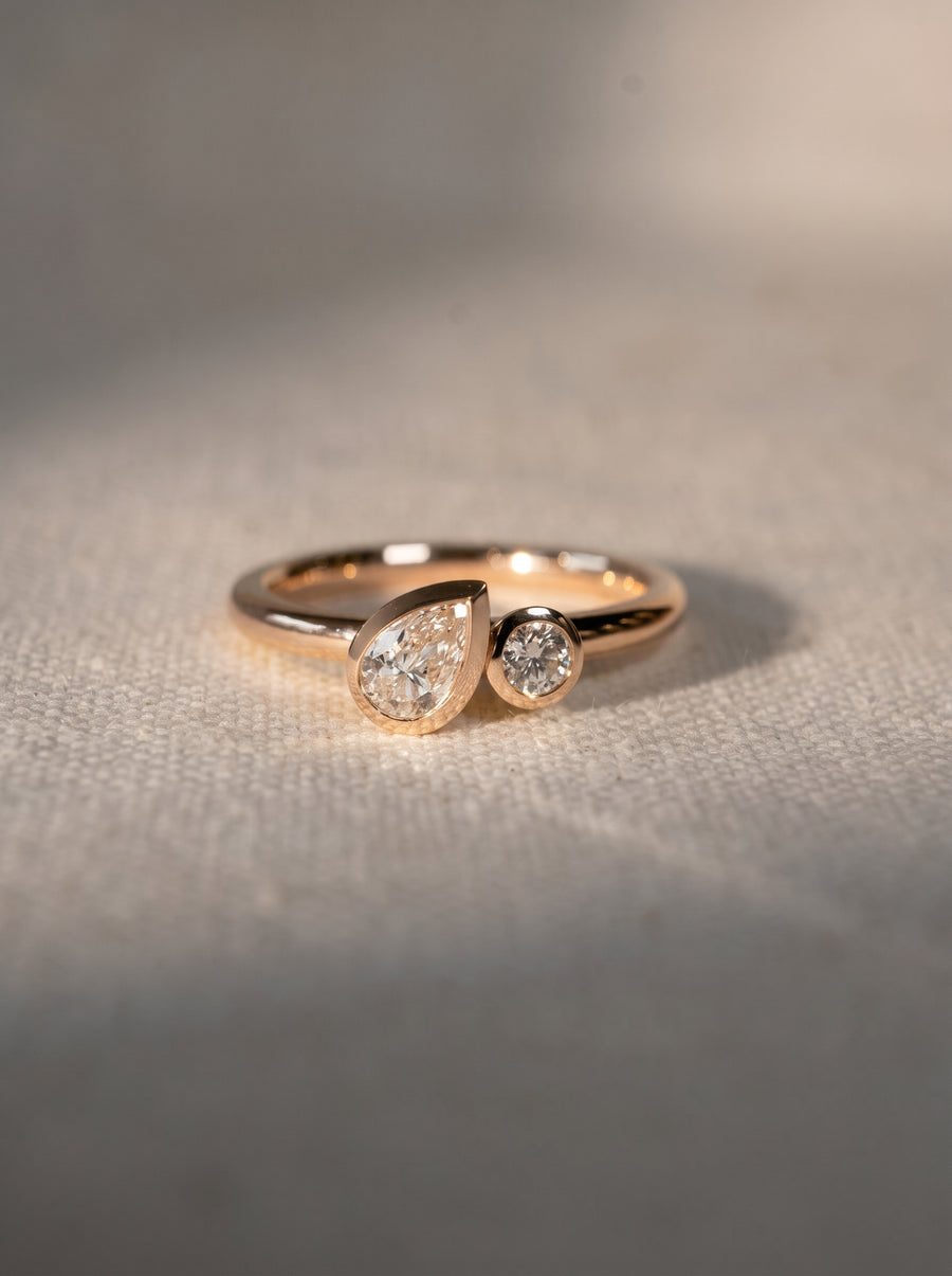 Rose gold toi et moi ring featuring a pear-shaped and a round diamond in bezel settings.