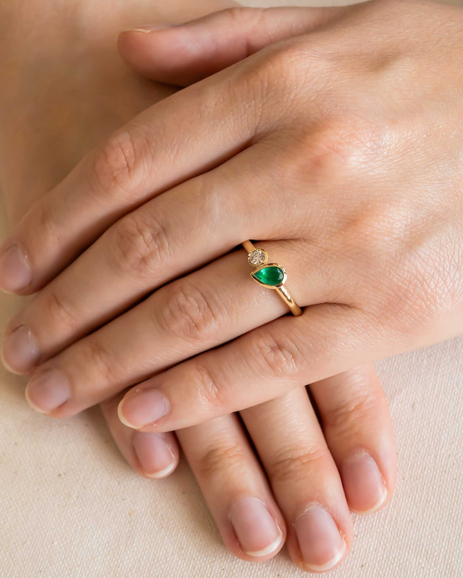 Gold Toi et Moi ring with pear emerald and round diamond on a hand.