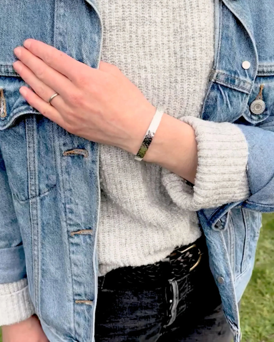 Person wearing a textured silver bangle bracelet, denim jacket, and grey knit sweater outdoors