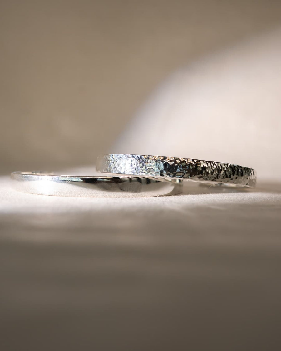 pair of silver bangle bracelets with hammered and polished textures on a soft fabric