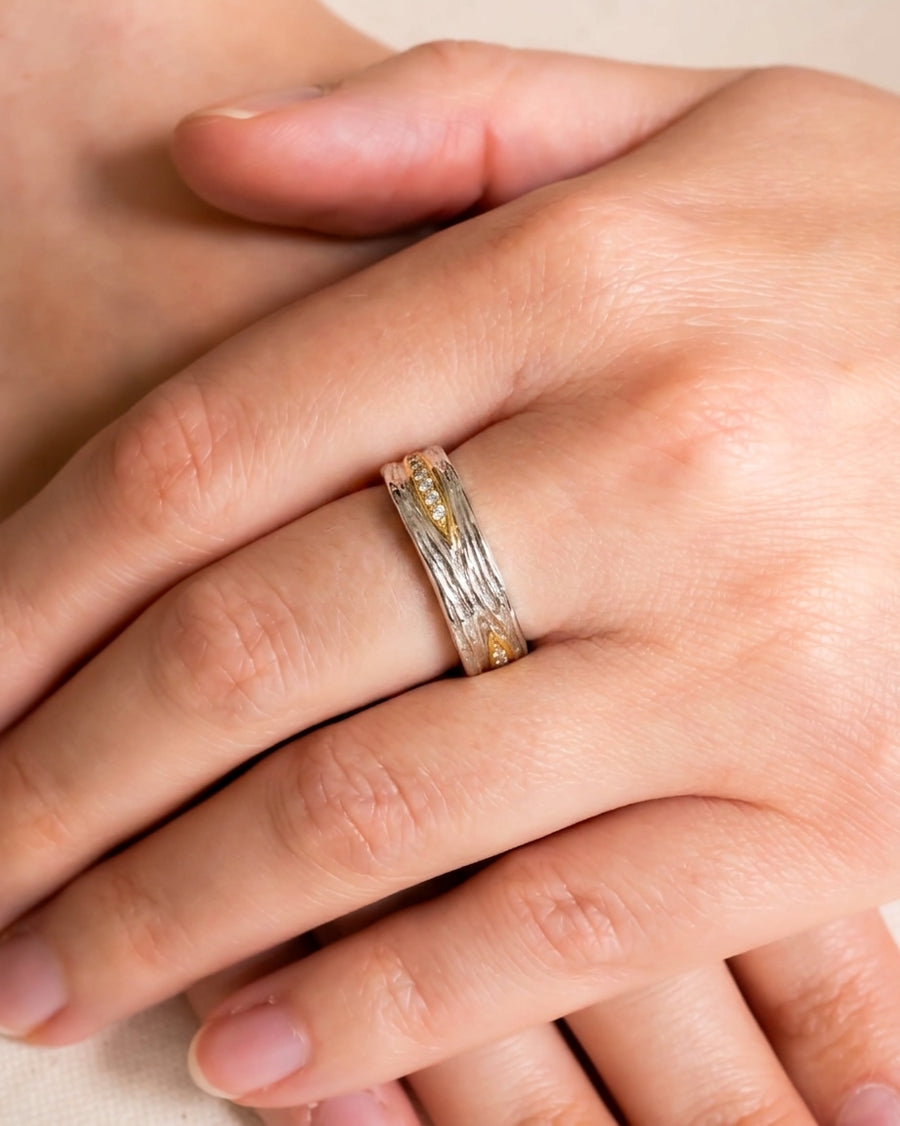 Two-colour carved ring with diamonds on a hand.