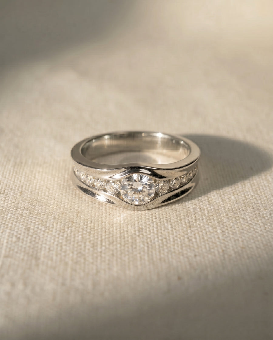 Platinum trap diamond engagement ring with a round center stone and pave diamonds.