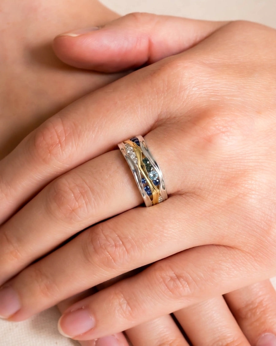Gold and silver eternity ring with green, blue sapphire, and diamond gemstones.