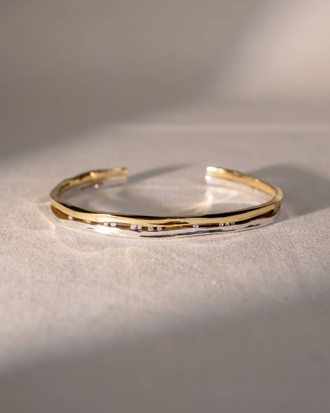 gold and silver cuff bangle with scattered diamonds on textured fabric background