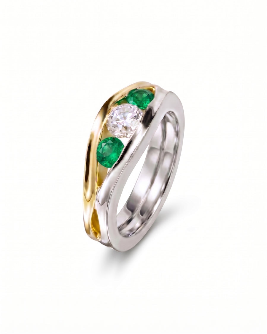 Two-tone gold ring with a central diamond and two emerald gemstones.