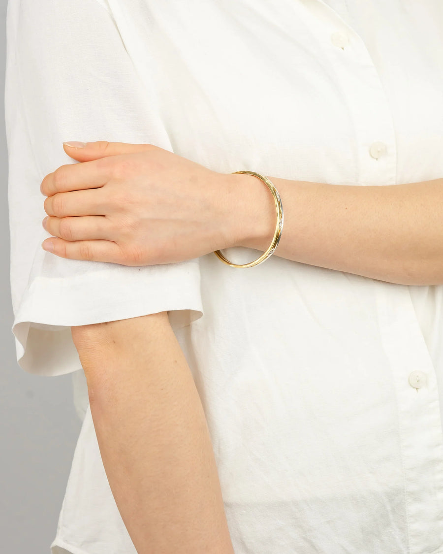 Handmade gold bangle with organic texture worn on wrist, white shirt background