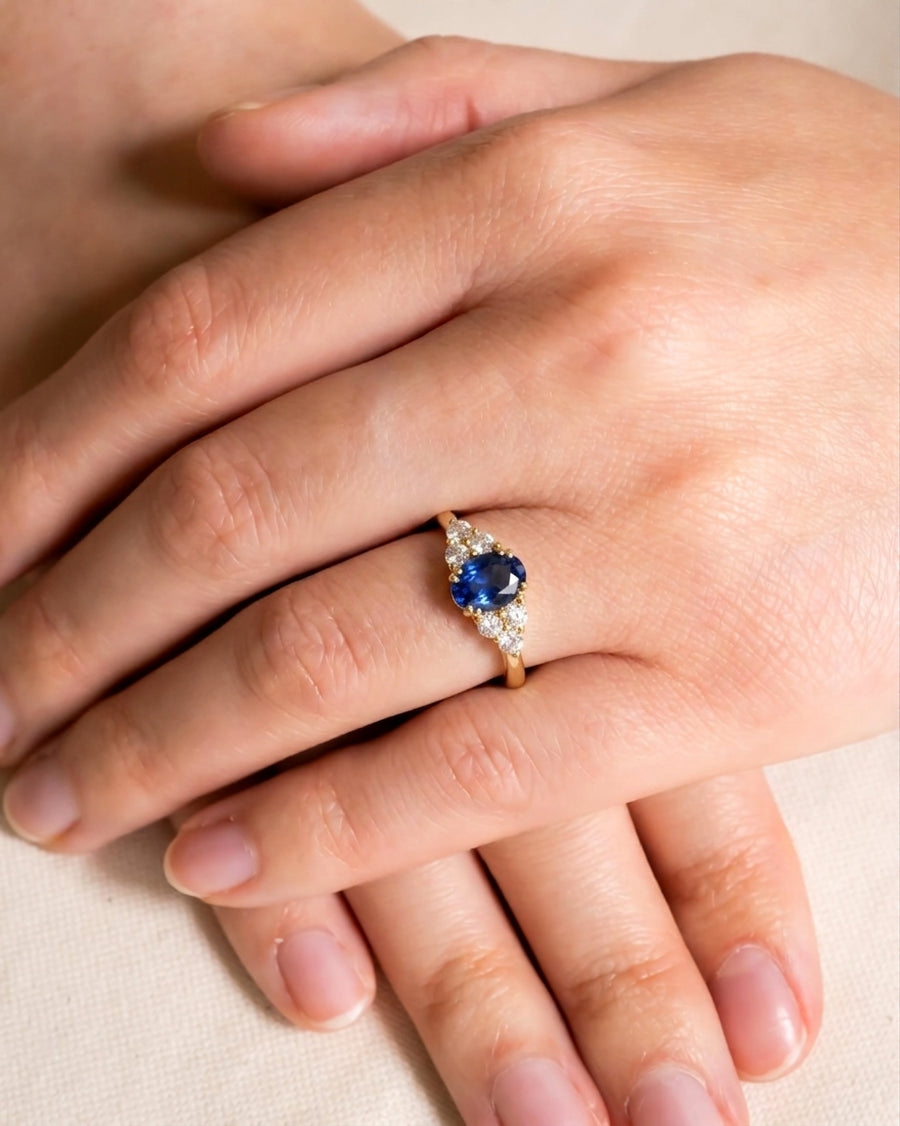 Gold ring with an oval sapphire and trefoil diamond clusters on a hand.