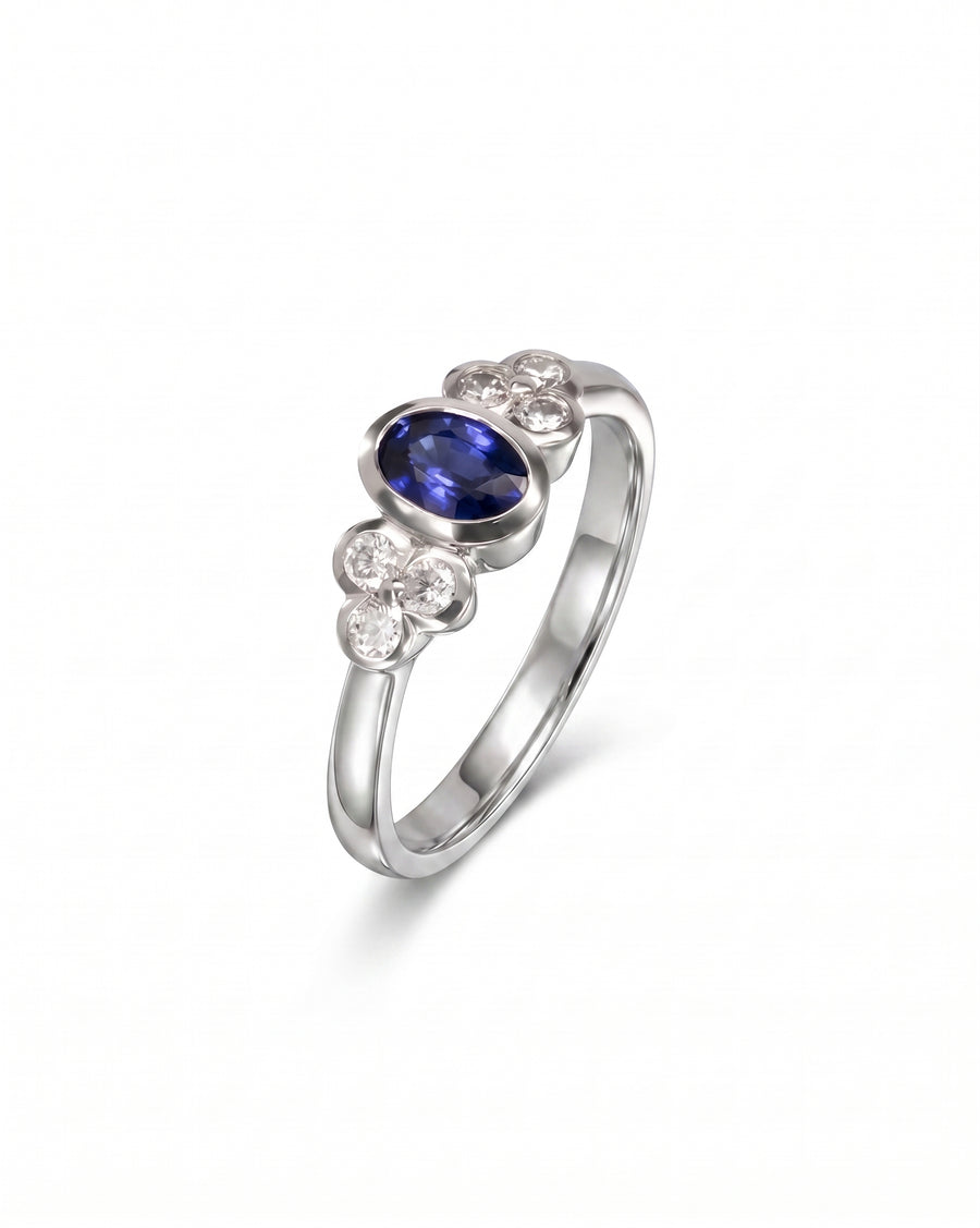 White gold engagement ring with an oval sapphire and six round diamonds in a trefoil design.