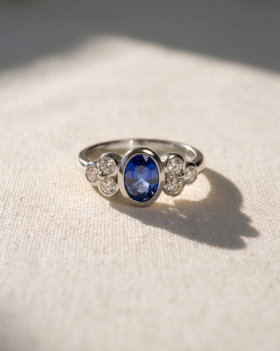 White gold engagement ring with an oval blue sapphire and trefoil diamond clusters.