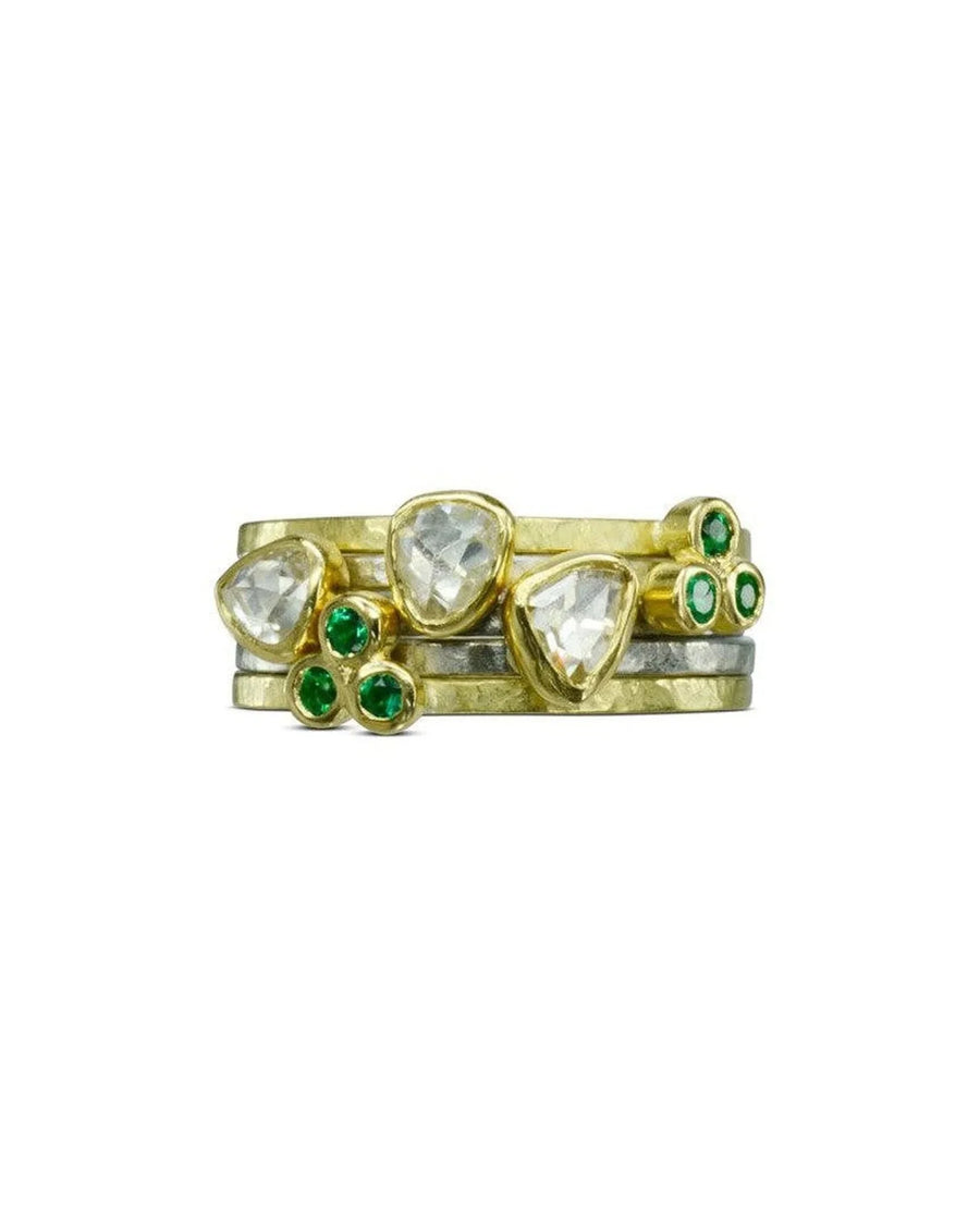 Gold stacking ring set with rough diamonds and green gemstone accents on white background