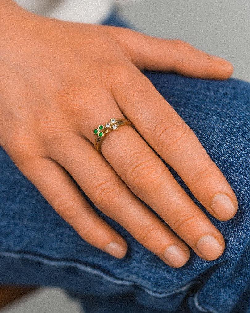 Gold stacking rings with green gemstones and rough diamonds on hand, stylish jewelry