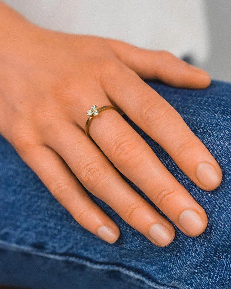 Gold ring with three small diamonds in a trefoil design on a hand.
