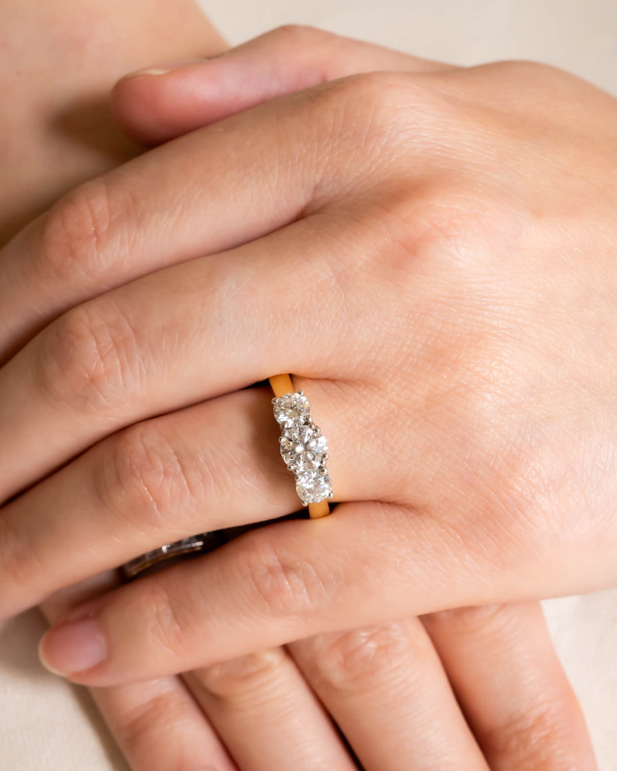Gold hinged engagement ring with three oval diamonds on a hand.