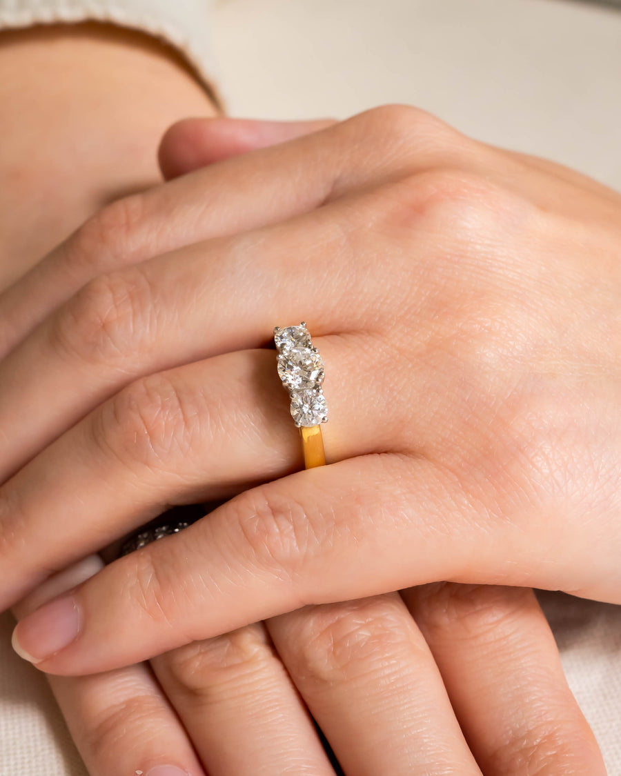 Gold hinged engagement ring with three round diamonds on a hand.