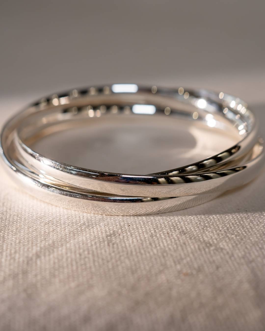 Handmade silver bangle bracelets with polished finish on textured fabric surface