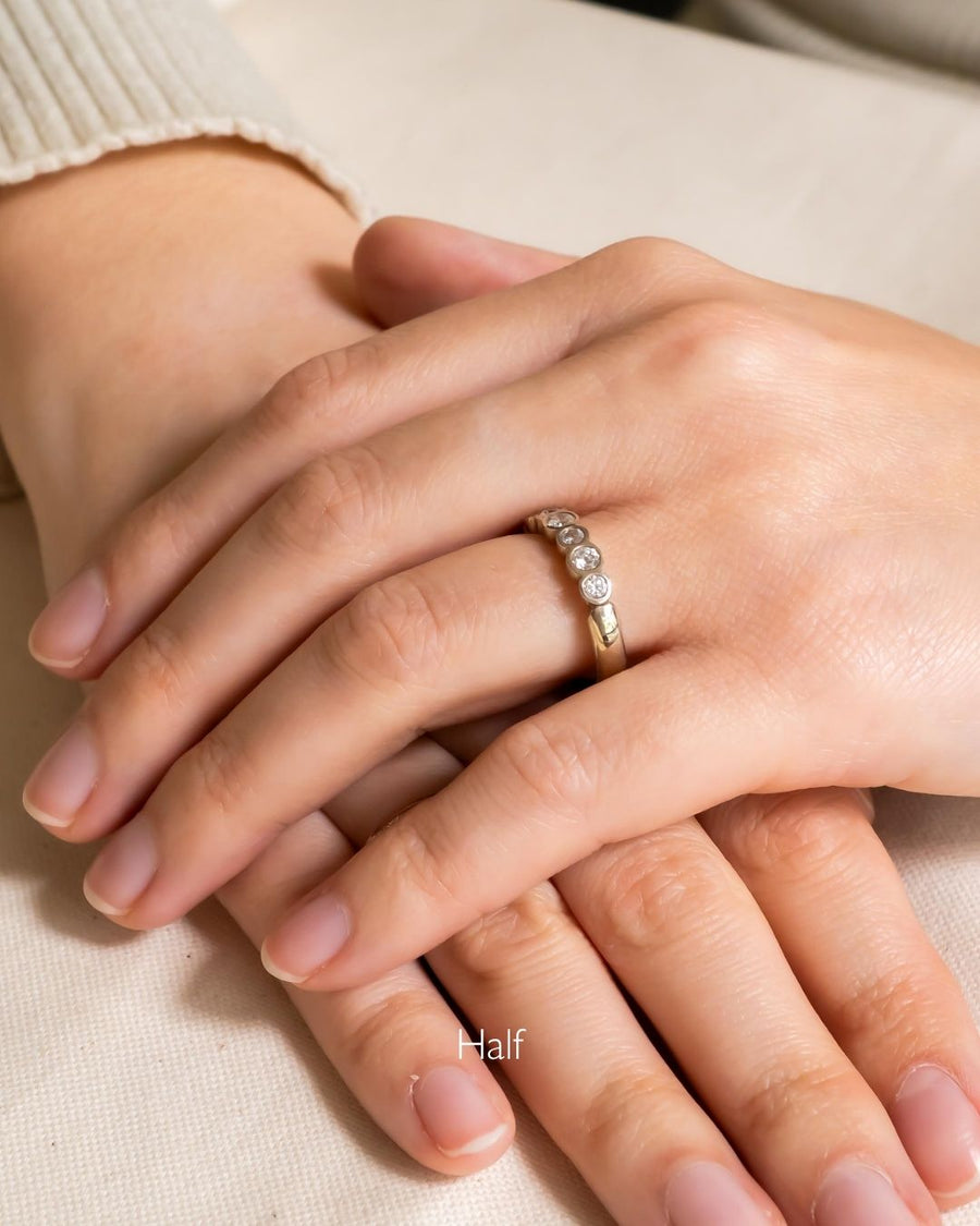 Gold band ring with five round diamonds on a person's hand.