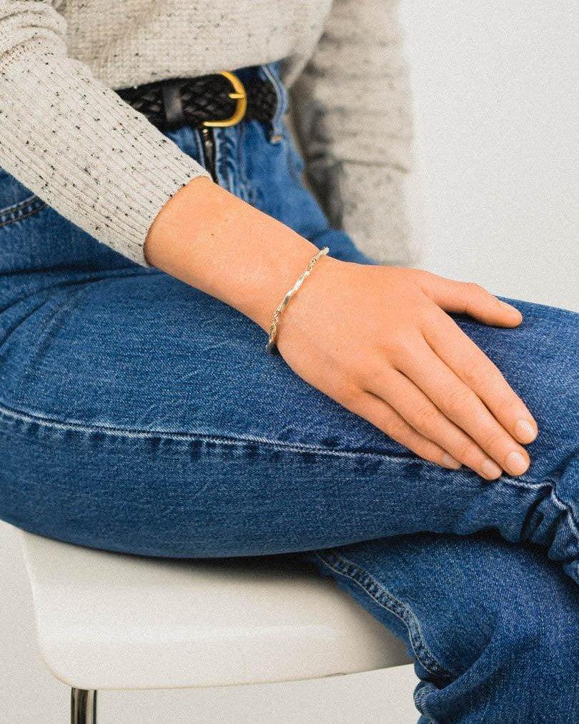Twisted silver bar bracelet worn on wrist, styled with casual jeans and a knit top