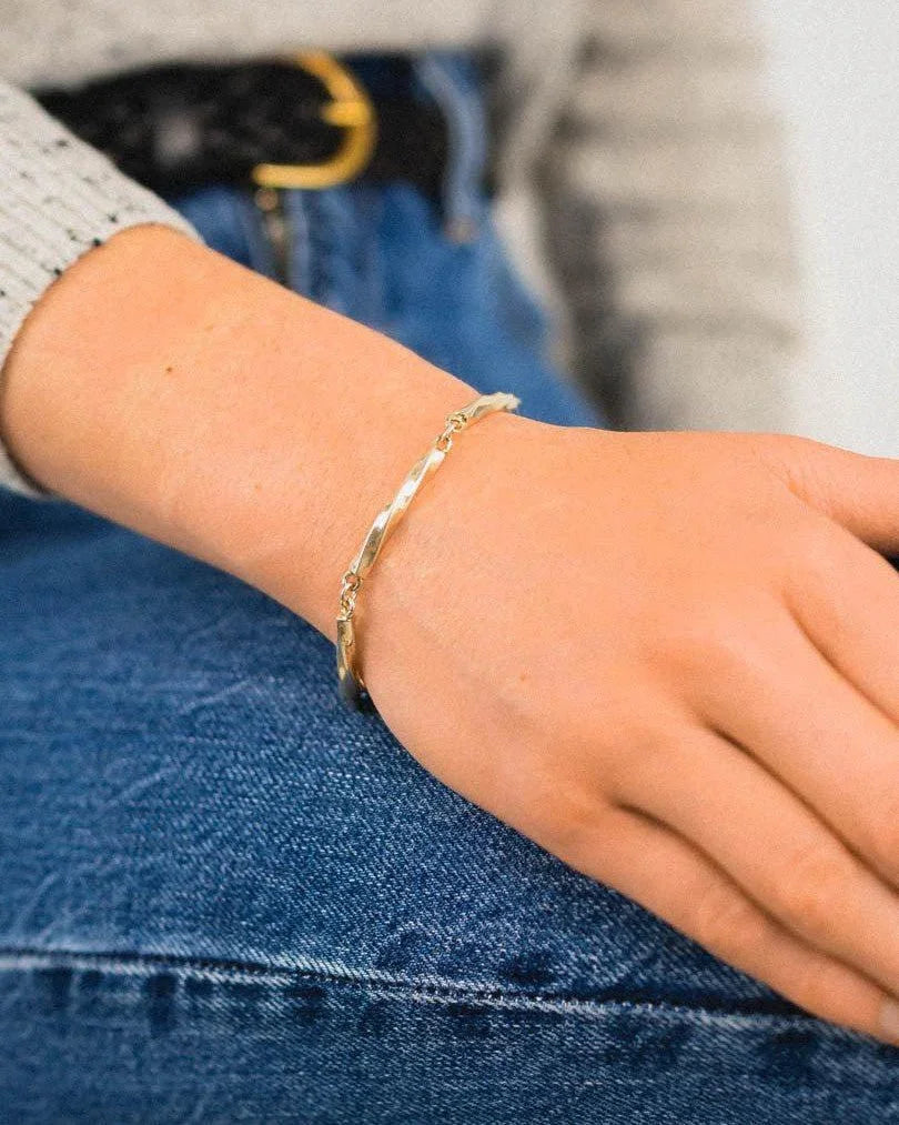 Hand wearing a twisted silver bar bracelet, styled with casual denim jeans