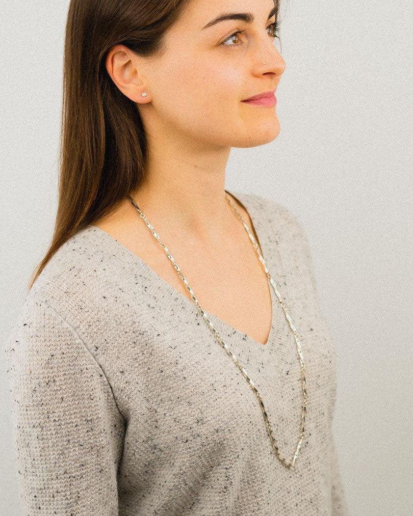 Woman wearing a long twisted silver chain necklace over a light knit sweater