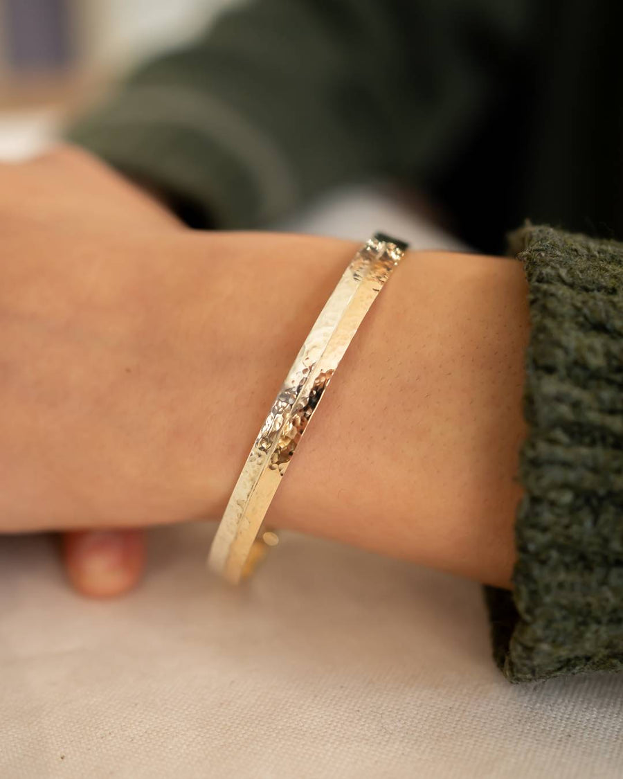 Two tone 9ct gold hammered bangle on a wrist.