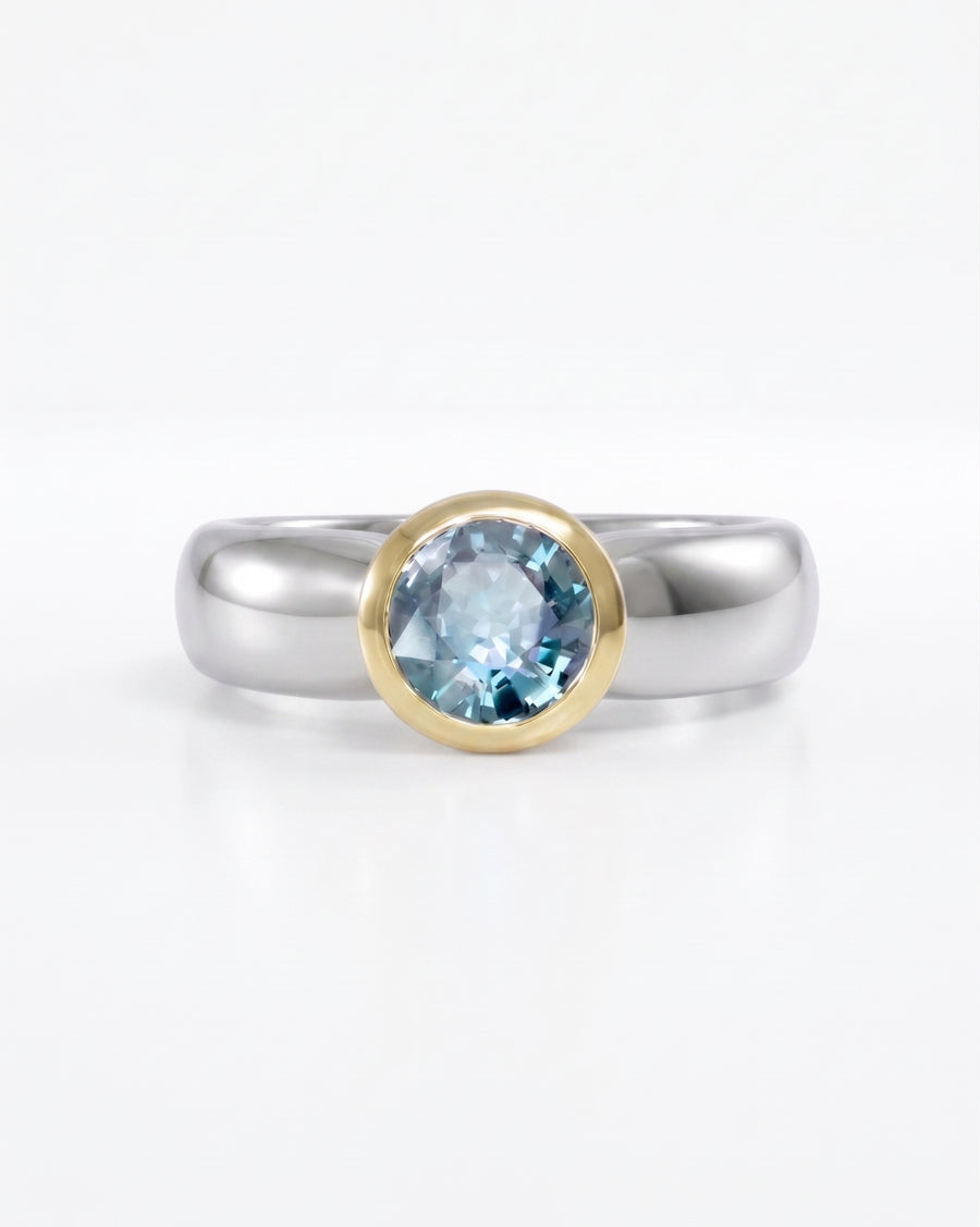 Two-tone engagement ring with a round blue gemstone in a gold bezel setting.