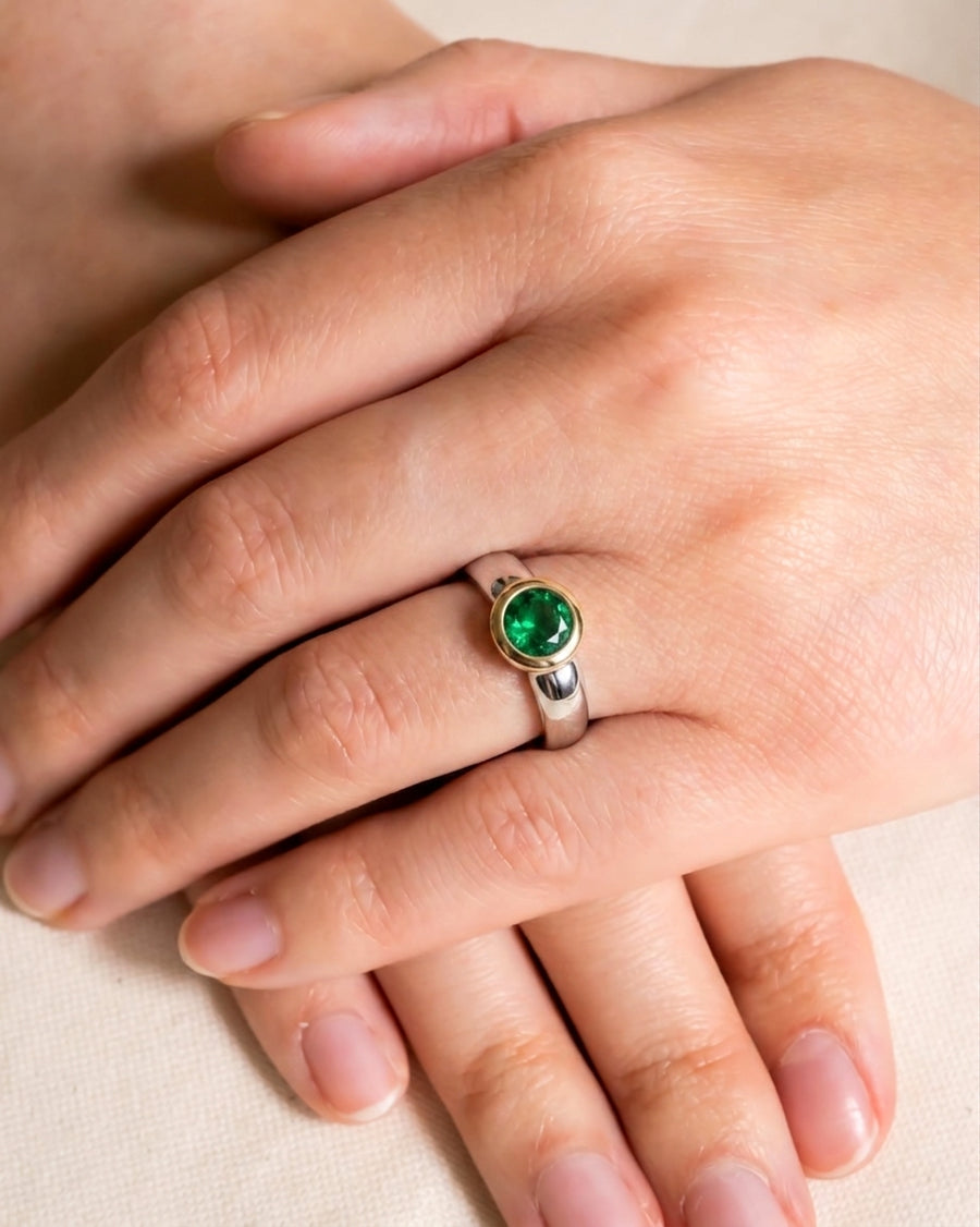 Two-tone engagement ring with a round green emerald in a gold bezel setting.