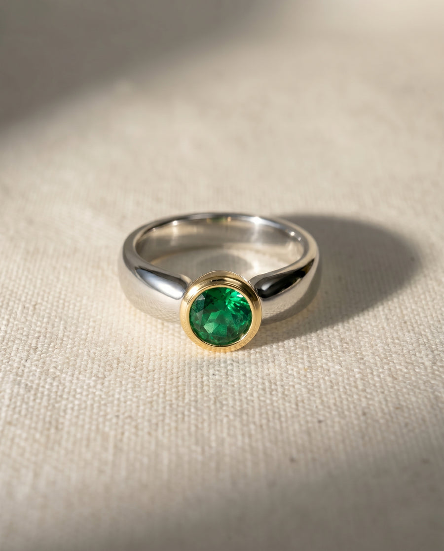 Two-tone engagement ring with an oval green gemstone in a gold bezel setting.