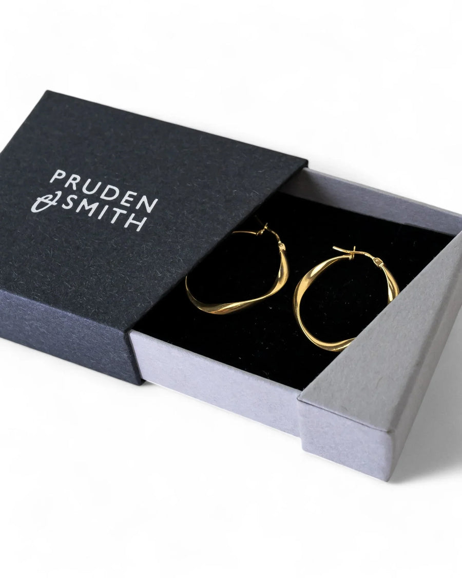 Uneven twisted gold hoop earrings with organic shape in a gift box on white background