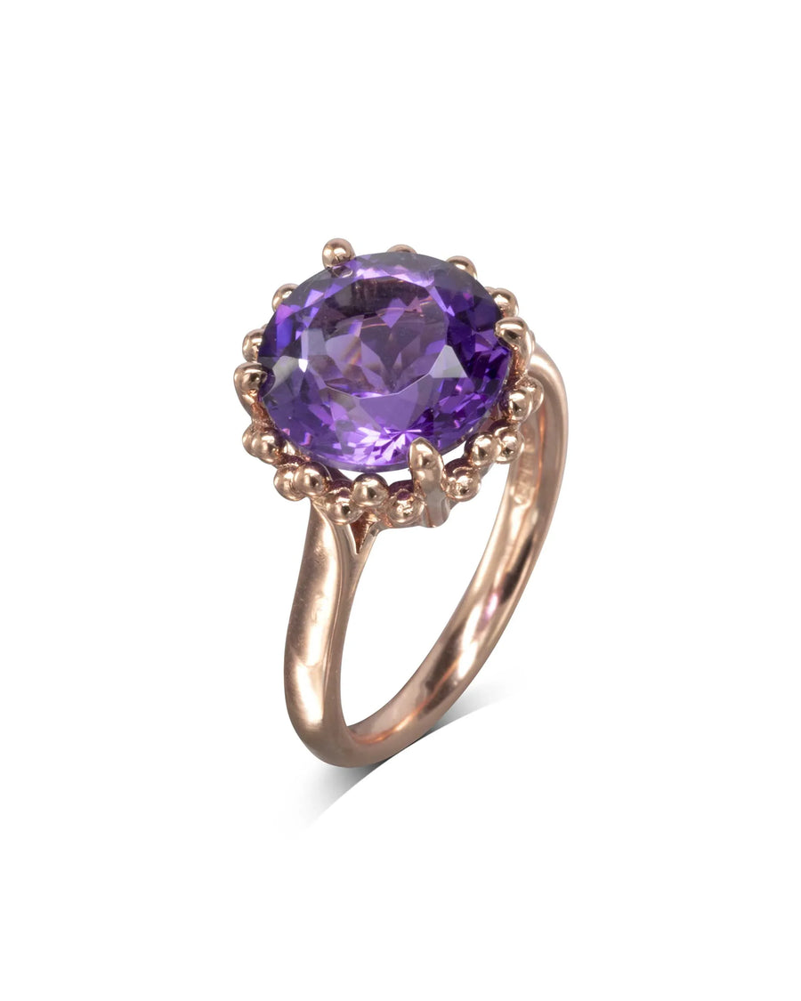 Gold ring with a large faceted amethyst and beaded detailing on white background