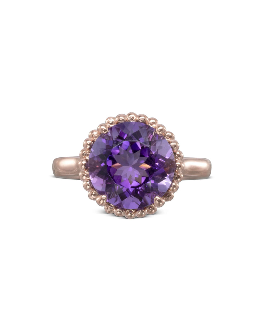 Rose gold ring with round amethyst gemstone and beaded halo design on white background